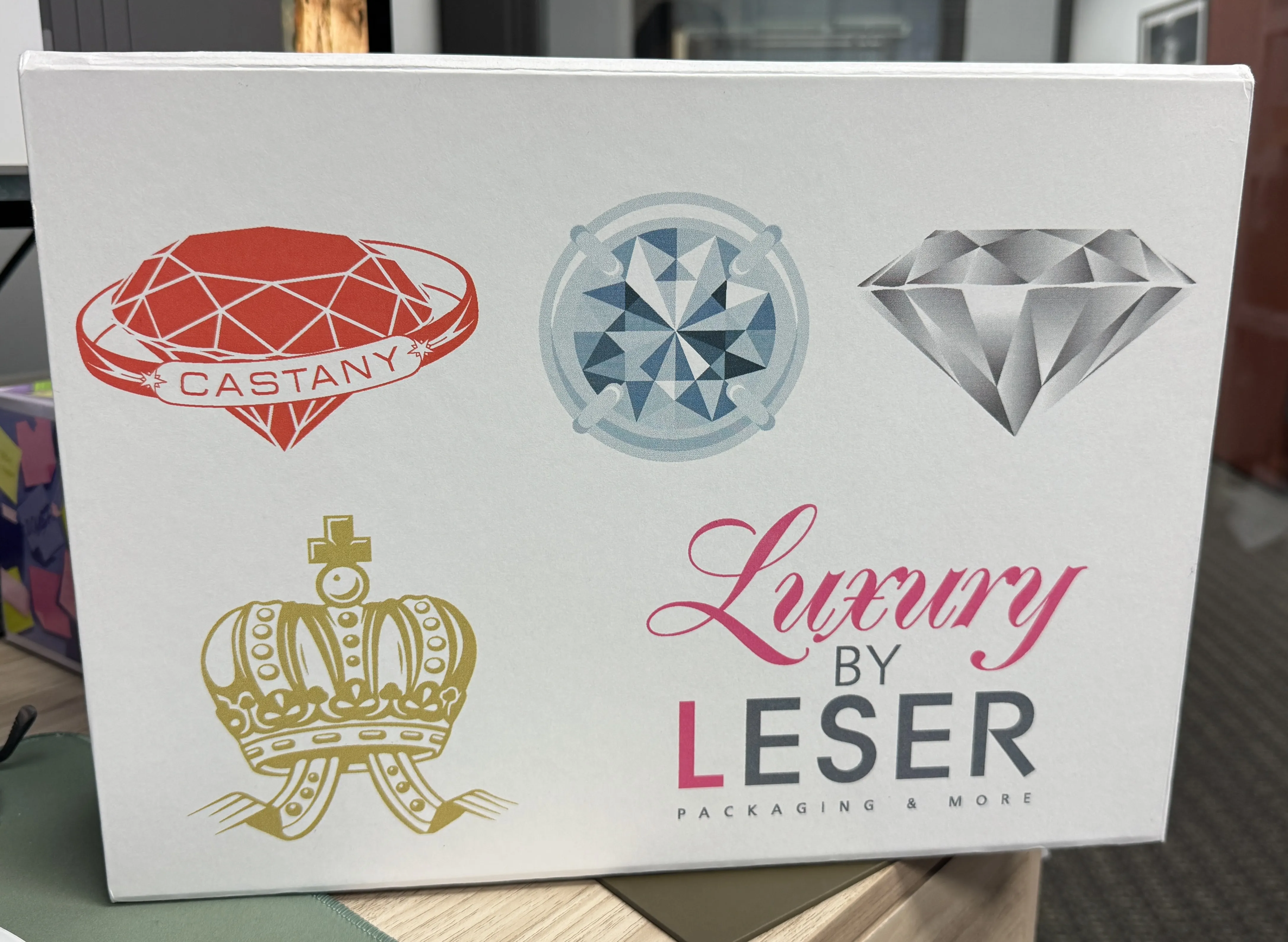 Vit förpackning med diamanter, krona och logotyper i rött, guld och silver