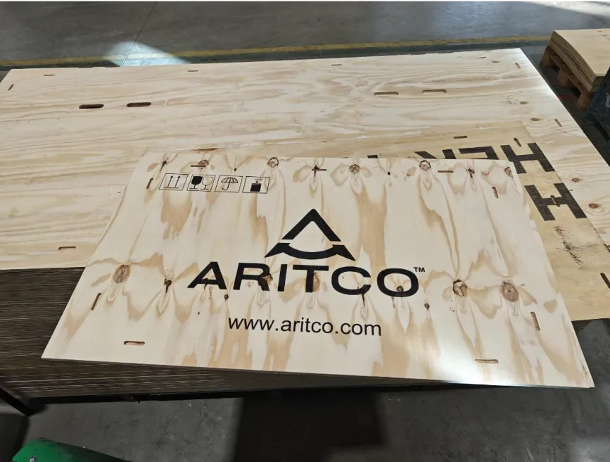 Plywoodskiva med Aritco-logotyp, webbadress och hanteringssymboler tryckta i svart